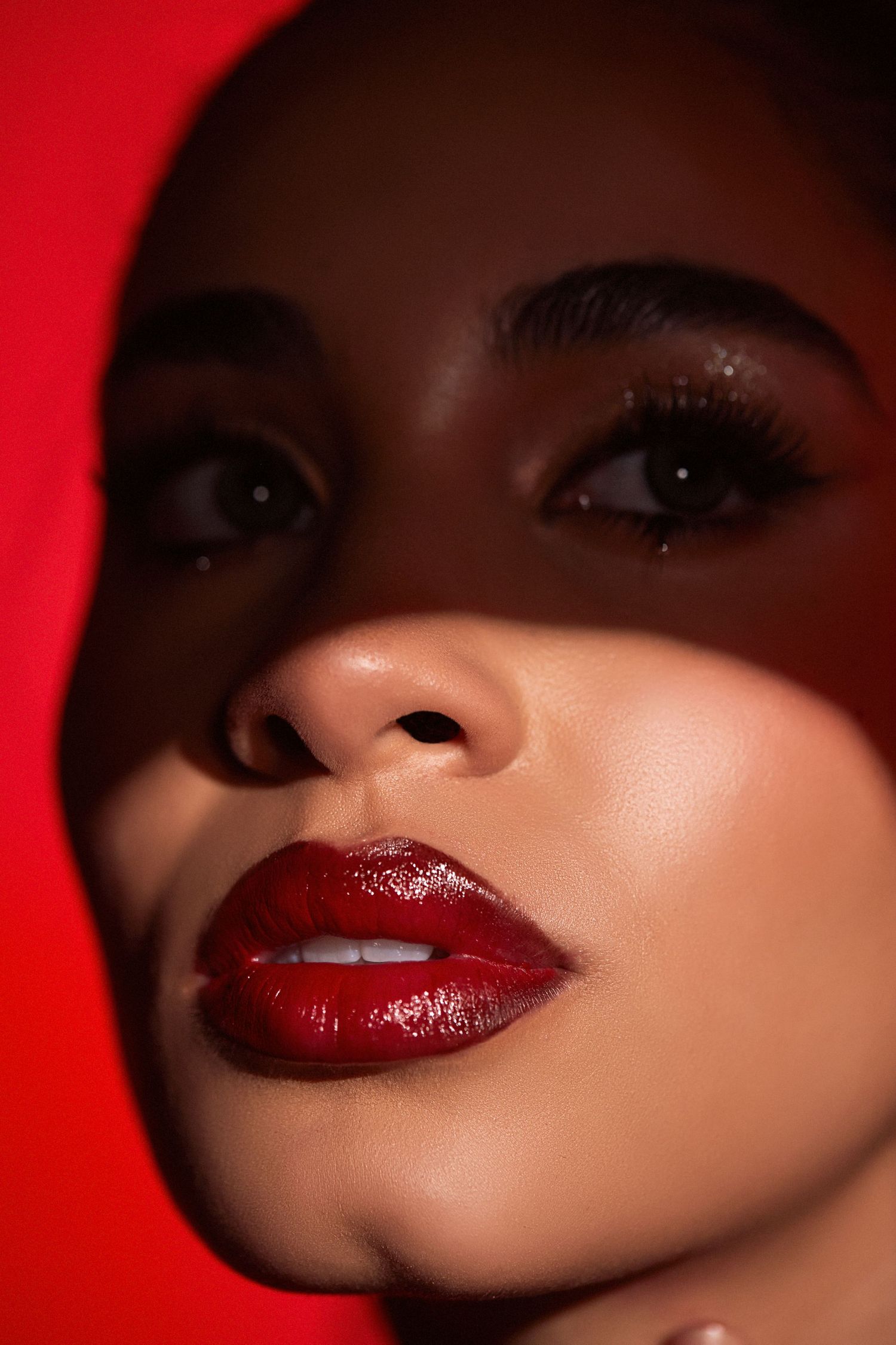 Dramatic beauty closeup with red lipstick and shadowed lighting against red backdrop.