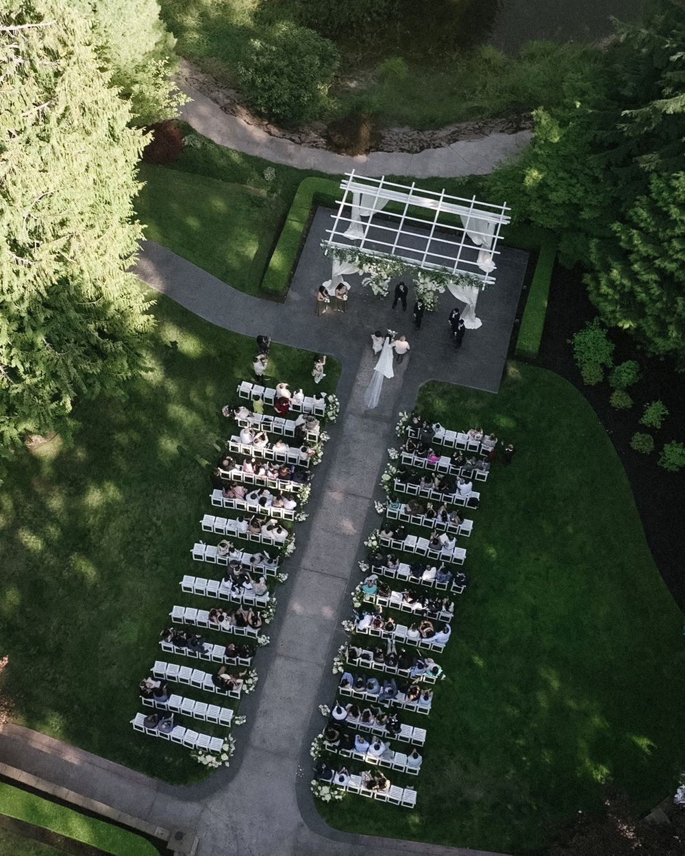 Aerial view of an outdoor wedding ceremony setup with white chairs arranged in rows surrounded by lush greenery.