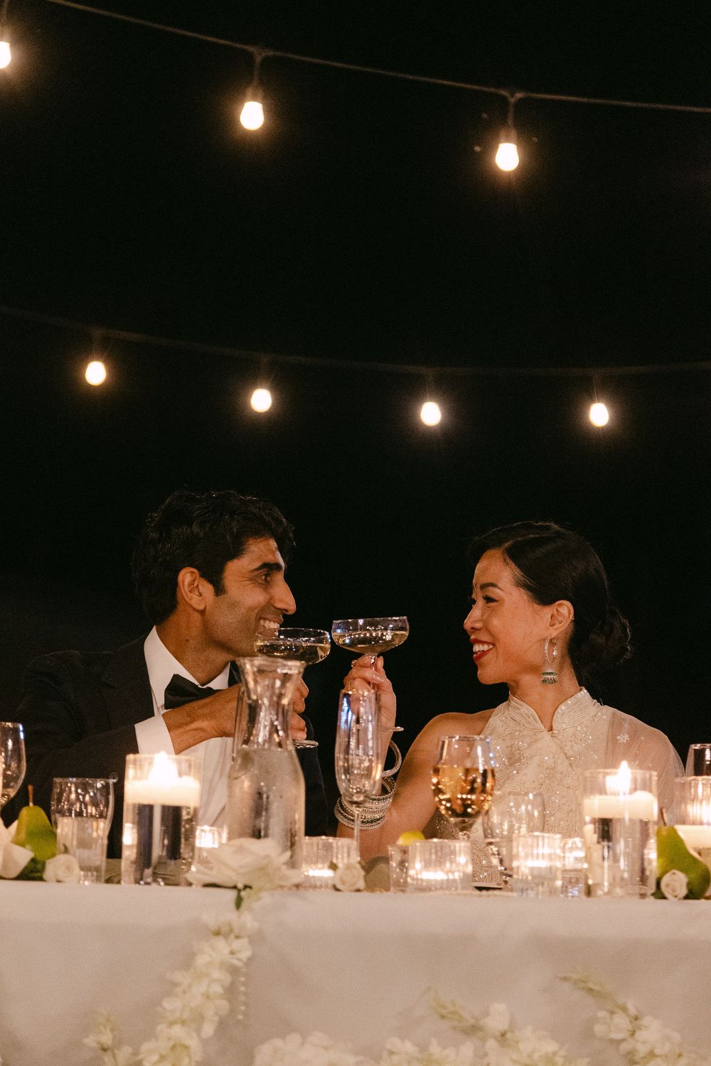 A romantic evening reception dinner under string lights with champagne glasses and table decor.