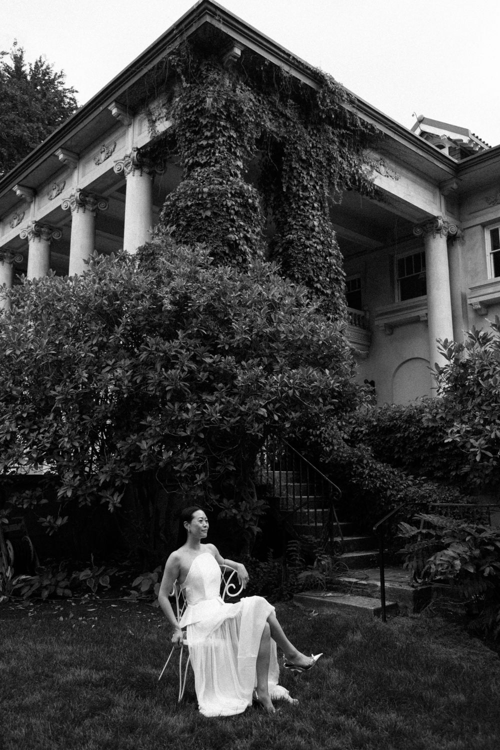 Person in white dress posing near an ivy-covered building with columns.