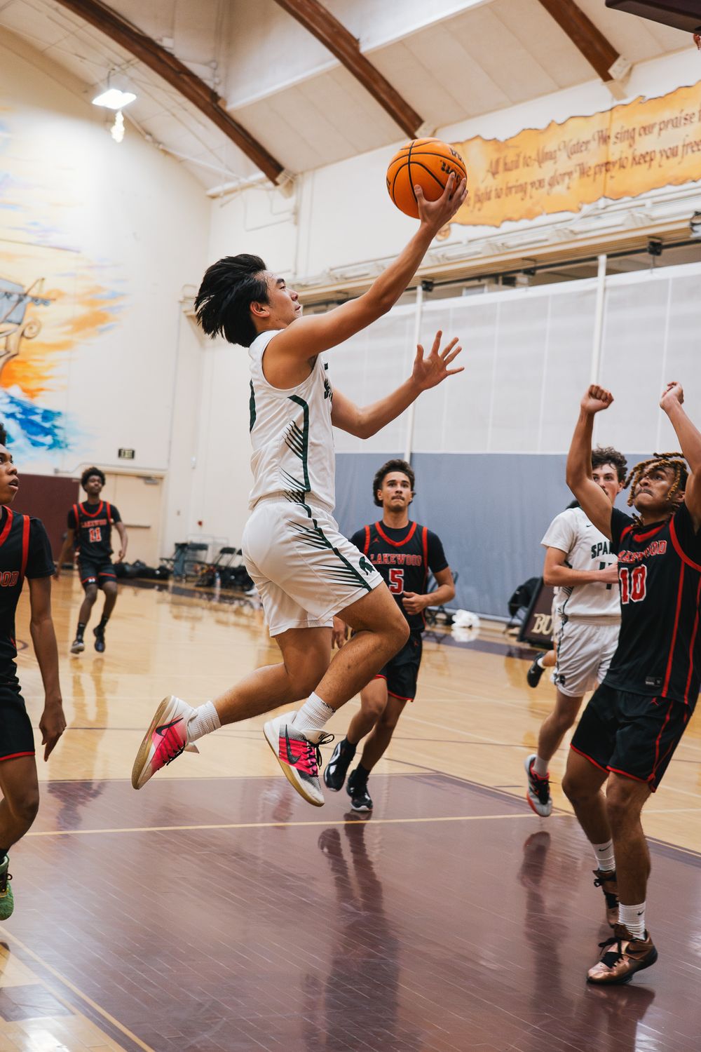 Basketball players jump and reach for the ball during an intense indoor game at a gymnasium.
