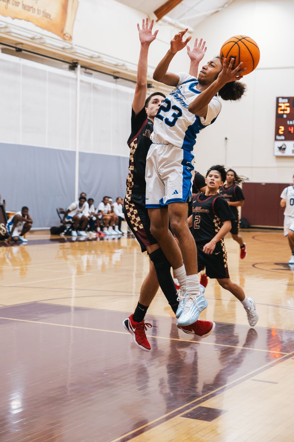 Basketball players leap and compete for possession during an intense indoor game on a wooden court.
