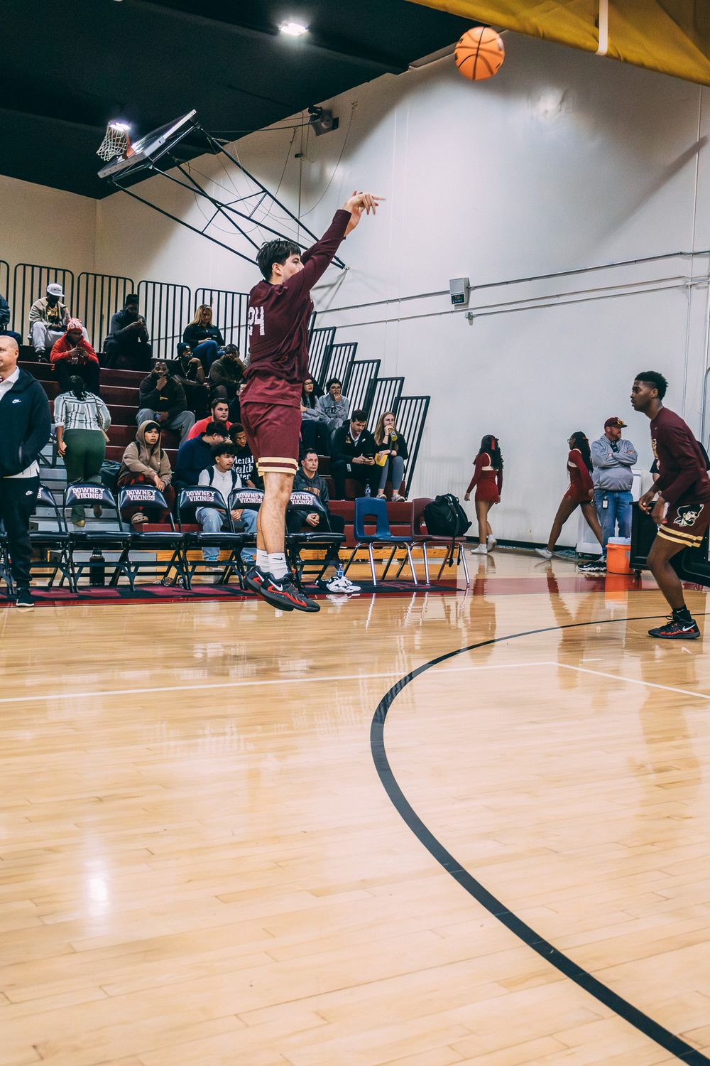 Basketball player jumps high to make a shot on an indoor court while others watch from the sidelines.