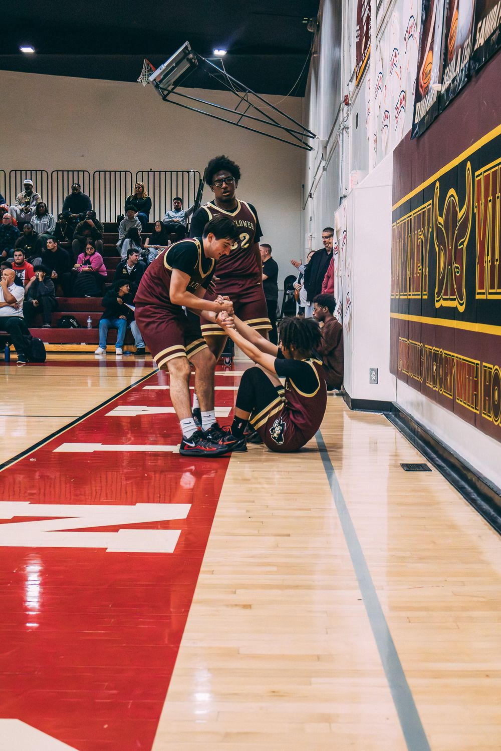 Basketball players helping teammate up from the court during indoor game.