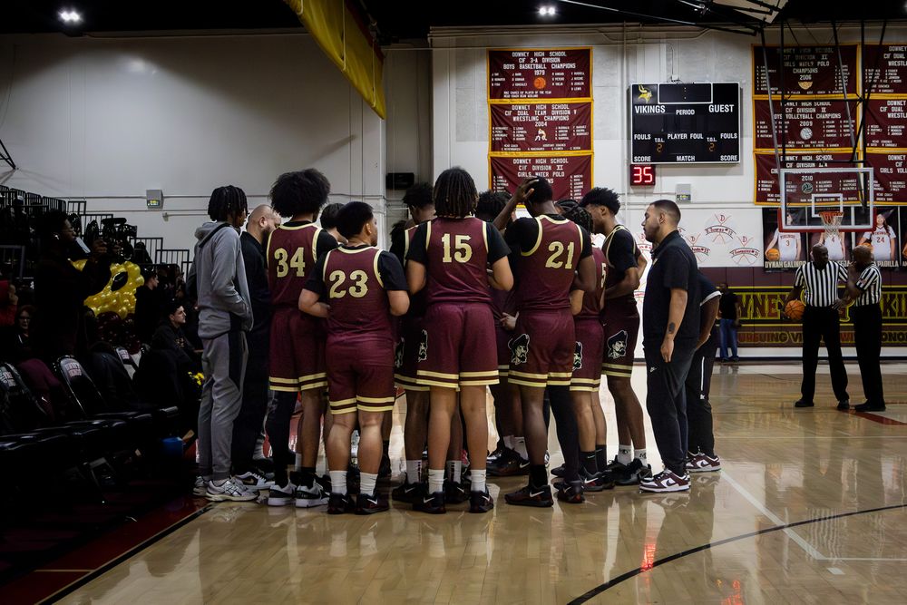 Basketball team huddles together during timeout with coaches on indoor court.