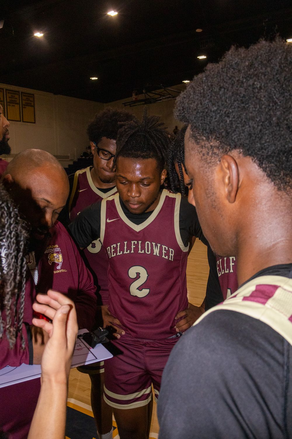 Basketball team huddles together wearing maroon jerseys during a game break.