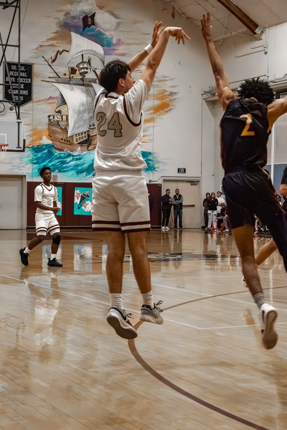 Multiple players leap and practice basketball moves on a shiny indoor court.