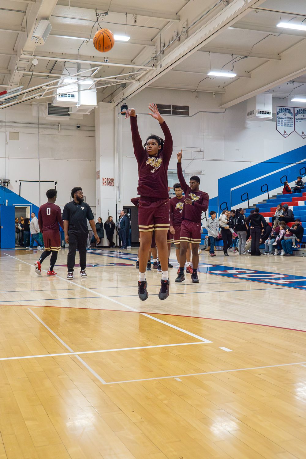 Basketball player in maroon uniform shoots jump shot on indoor court.