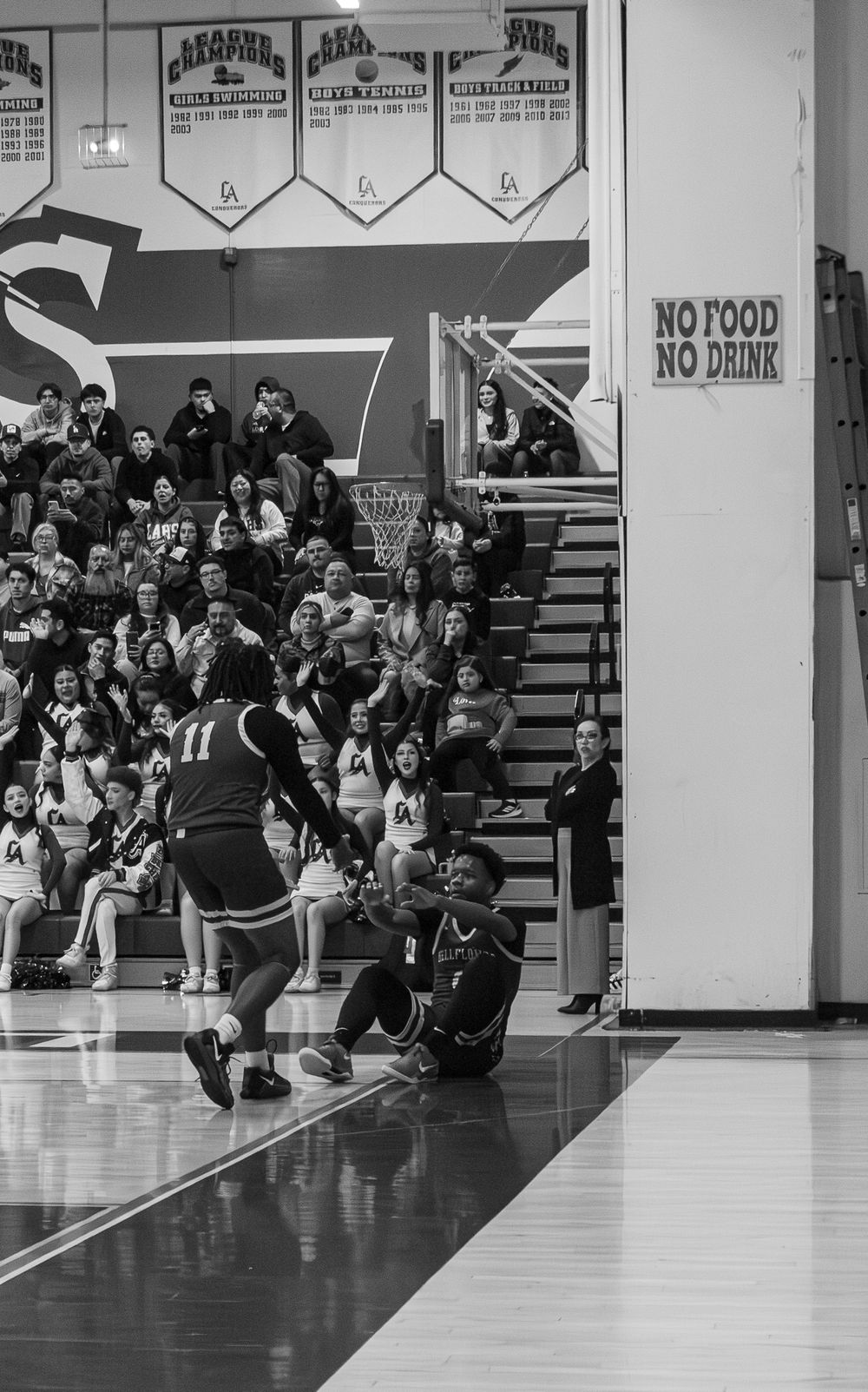Black and white photo of basketball game action in gymnasium with crowd watching.