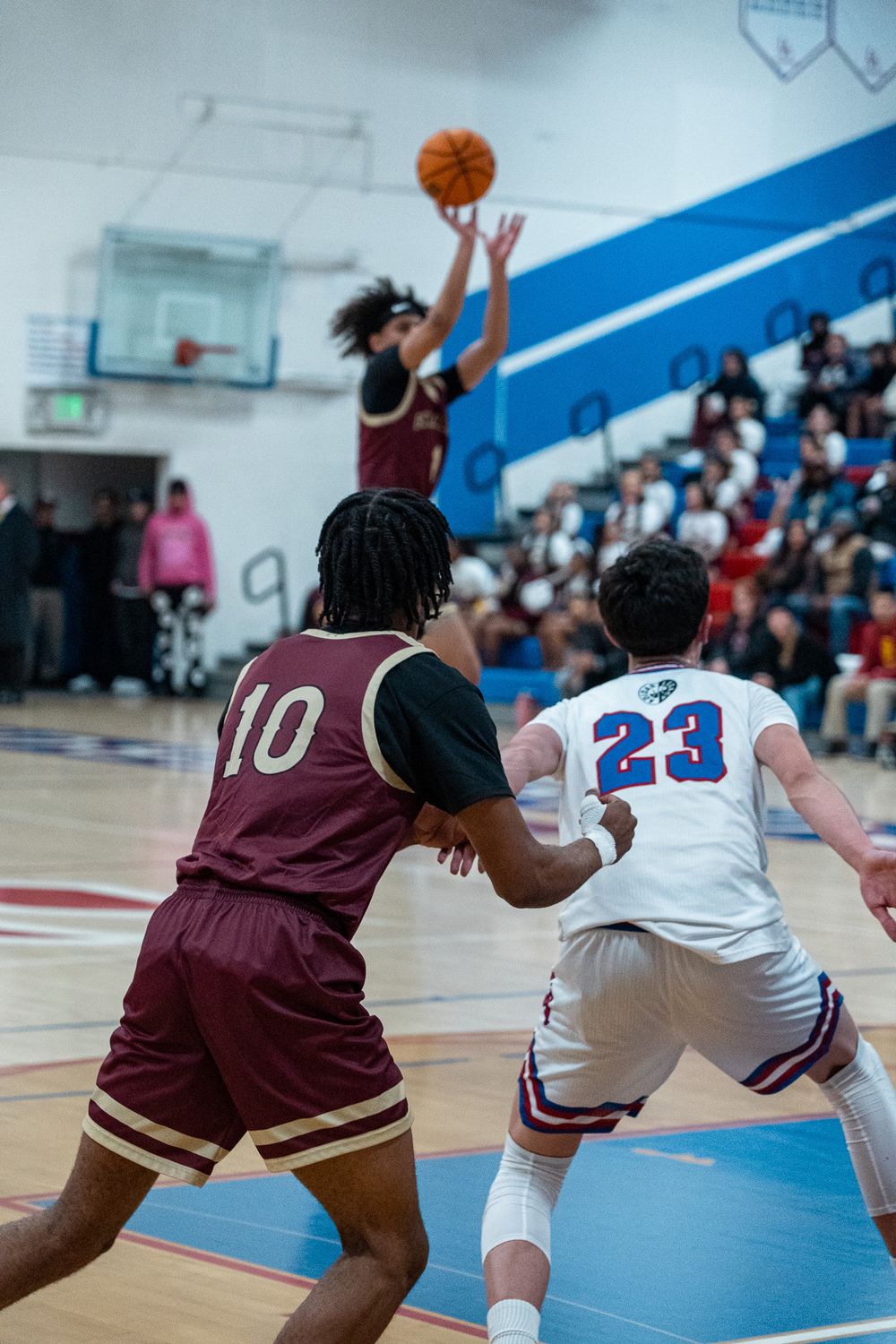 Basketball players compete for a rebound during intense game action on indoor court.