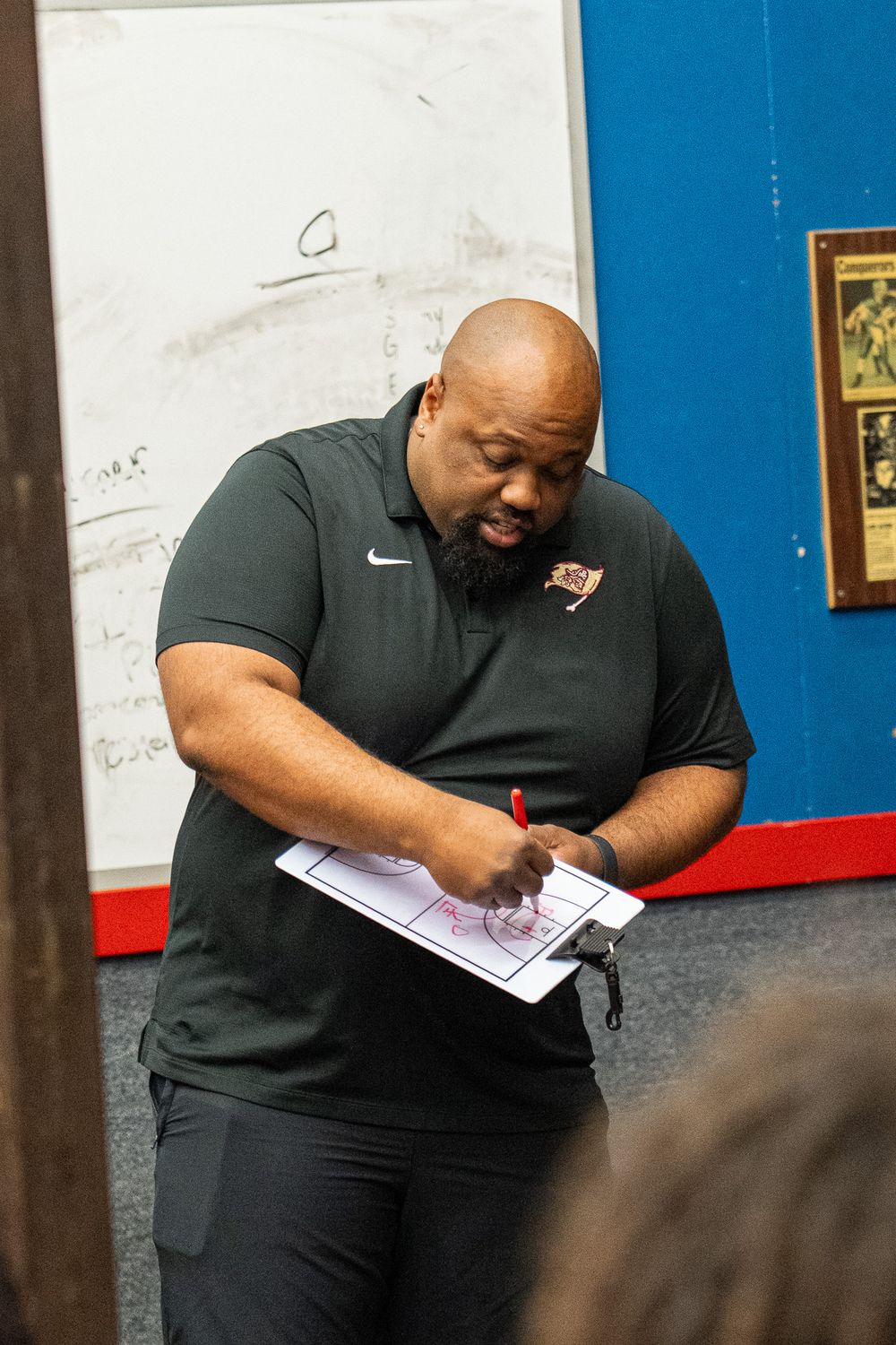 Coach in dark polo shirt reviews notes during basketball game.