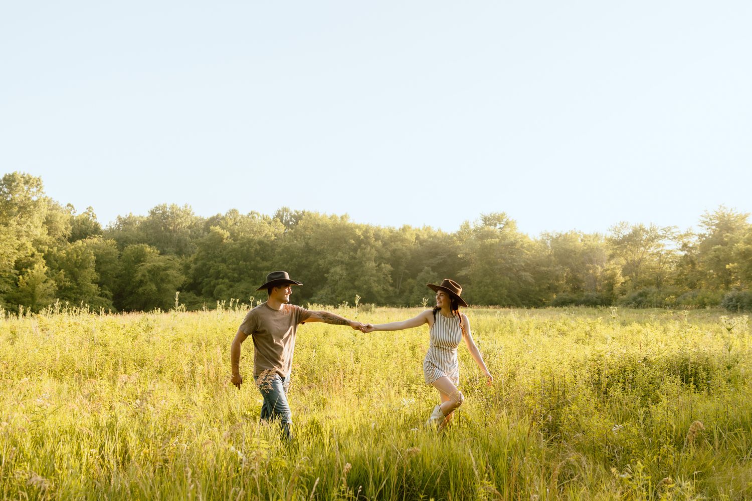 Couple shares romantic moment kissing on sunlit green hillside surrounded by trees in golden light.