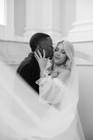 A romantic black and white wedding portrait showing an intimate moment between newlyweds with flowing white veil.