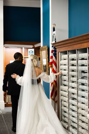 A bride and groom check their mailboxes in front of a wall of metal mailboxes in a sequential photo series.