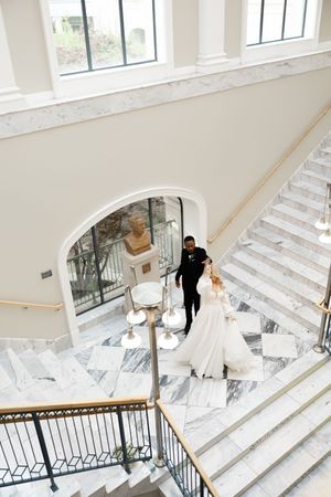 Elegant marble staircase in a bright white interior with an ornate railing and floor-to-ceiling windows.