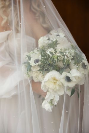 A delicate bridal bouquet of white anemones and seasonal flowers behind a sheer veil.