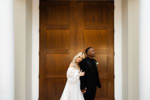 Bride and groom stand together against a grand wooden door at their wedding ceremony.