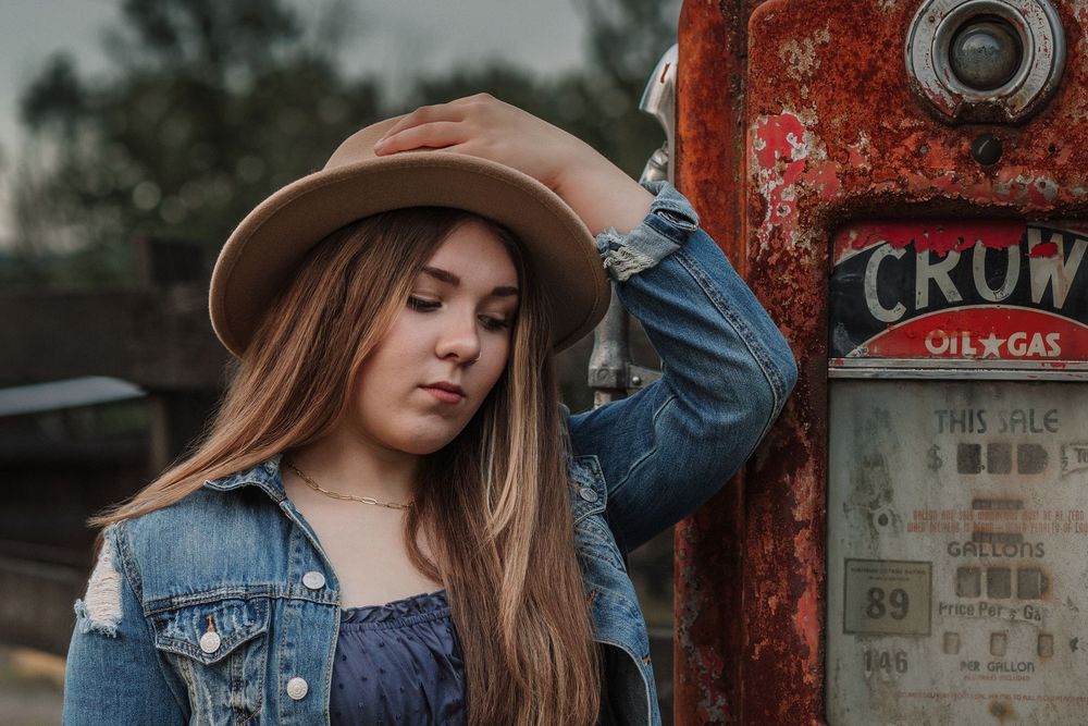 Moody portrait against vintage red gas station backdrop with rustic aesthetic.