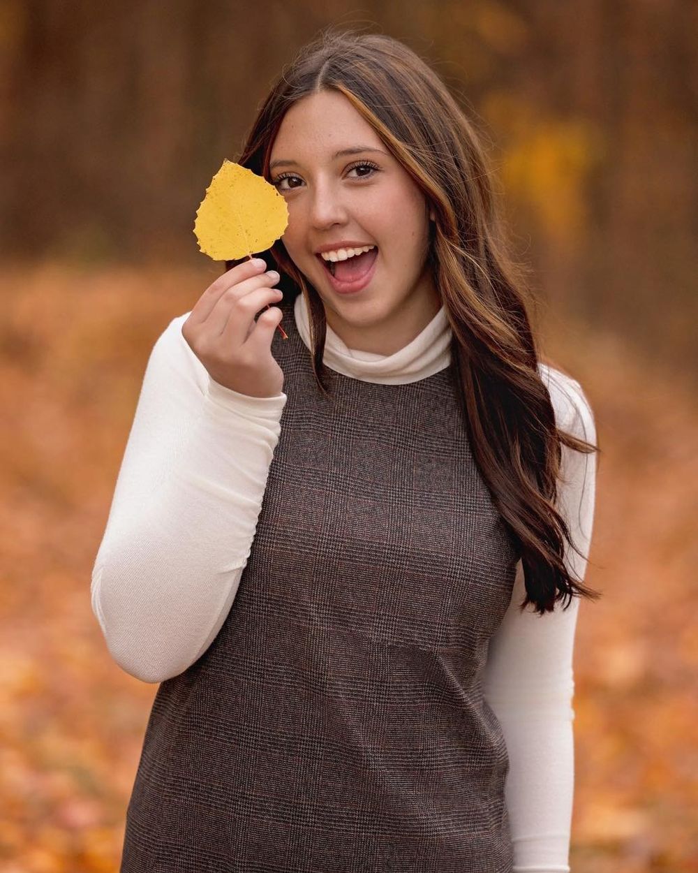 Autumn portrait featuring someone in a brown turtleneck and white sleeves holding yellow leaves.