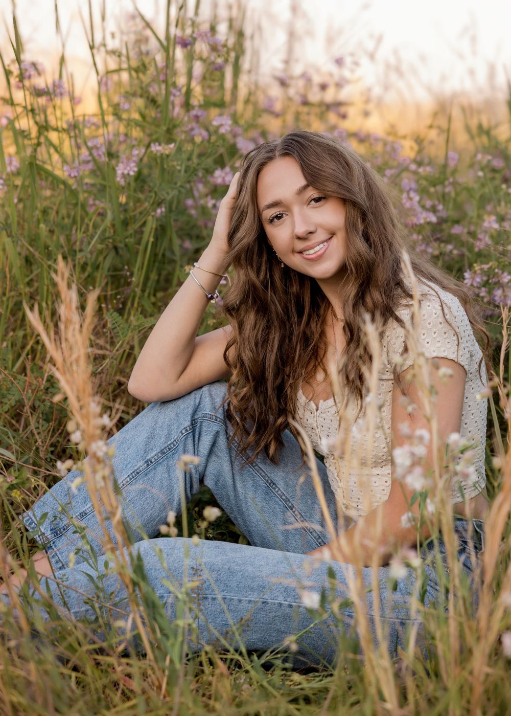 Person in denim outfit relaxes among wildflowers during golden hour photography session.