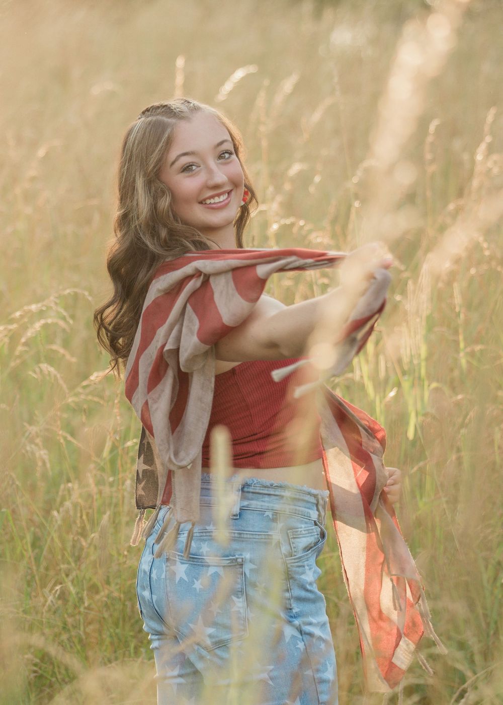 Person in denim and red top dances through tall grass during golden hour photoshoot.