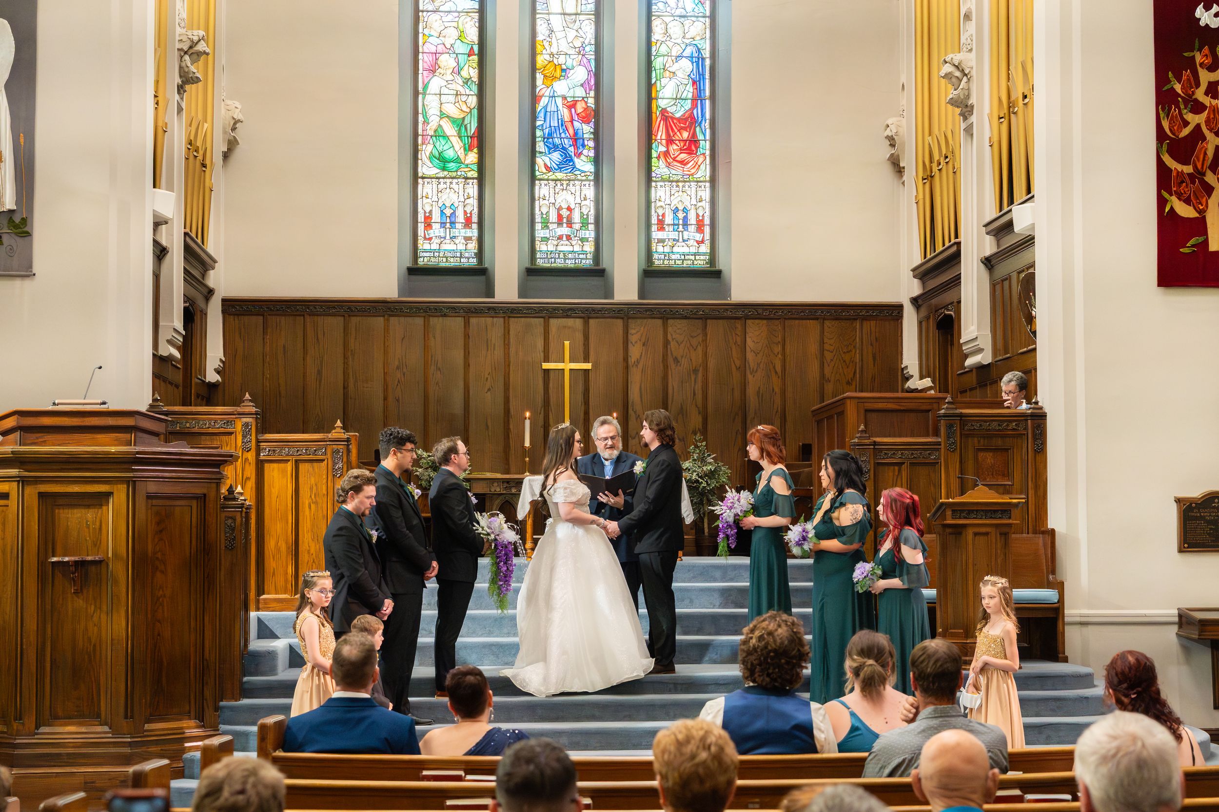 Wedding ceremony takes place in a traditional church with wooden pews and stained glass windows.