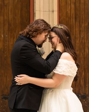 A romantic moment between a couple in wedding attire embracing against a rustic wooden wall background.