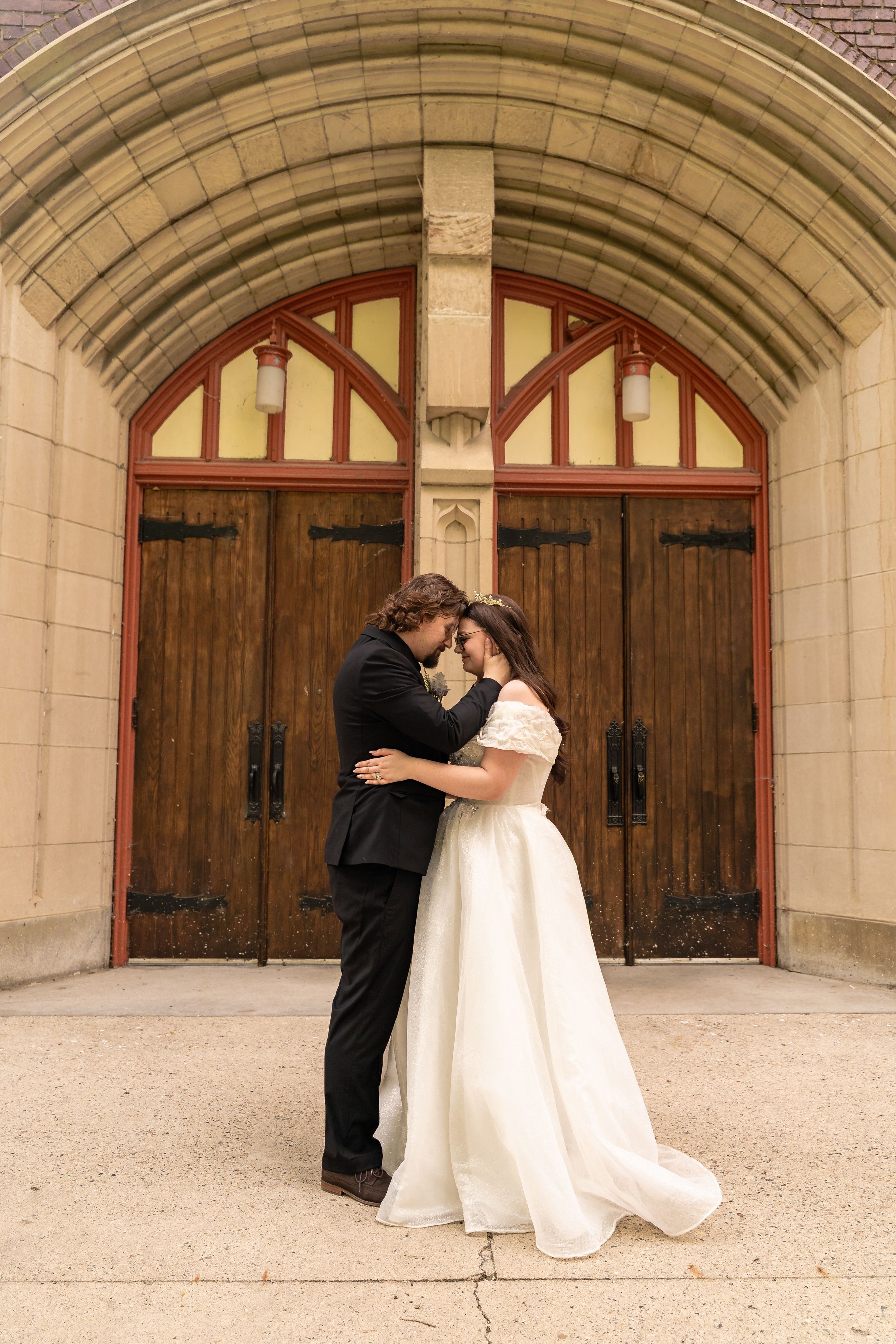 Wedding couple shares romantic moments under stone archway with wooden doors in elegant venue sequence.