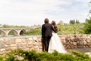 A couple in wedding attire stands at a stone wall overlooking an elegant arched bridge on their special day.