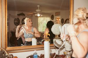 Bridal preparation scene with natural light streaming through windows as makeup is being done at a vanity with mirror.