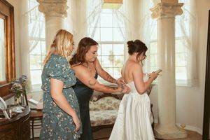 Bridesmaids in blue dresses helping with wedding preparations in a bright room.