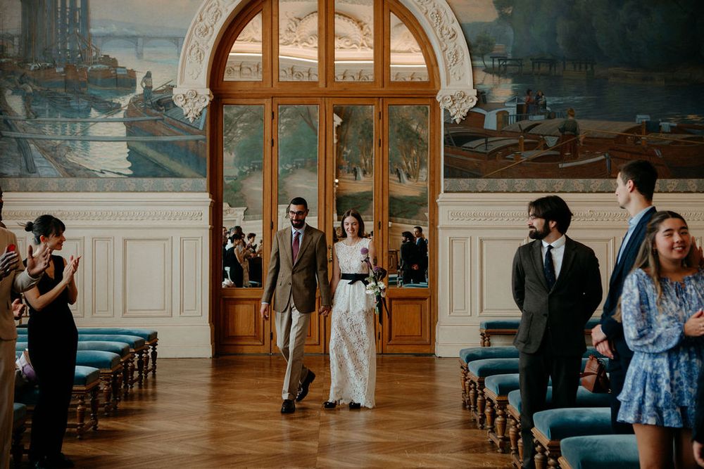 Newlywed couple walking hand in hand down the aisle after civil wedding ceremony in ornate French venue.