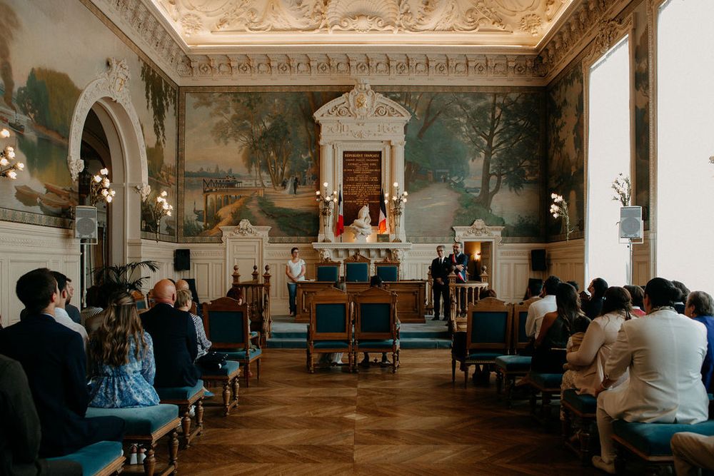 Wide view of elegant wedding ceremony room with pastoral murals, blue chairs, and couple at decorated altar.