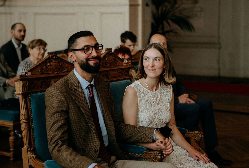 Smiling bride and groom seated in ornate blue velvet chairs during their intimate civil wedding ceremony.