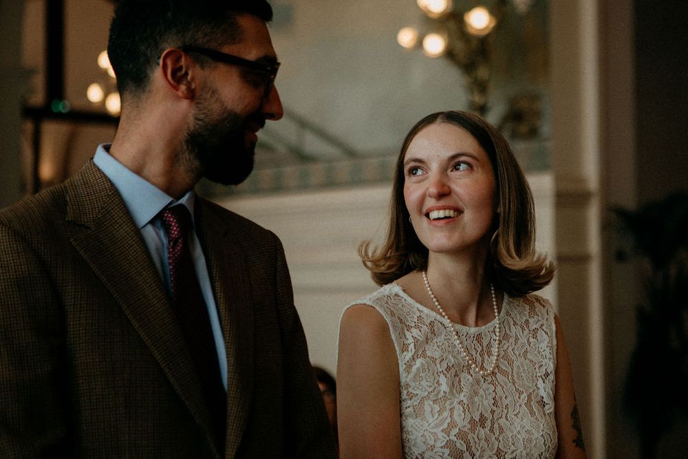 Bride smiles warmly at groom during intimate wedding ceremony in a softly lit venue.