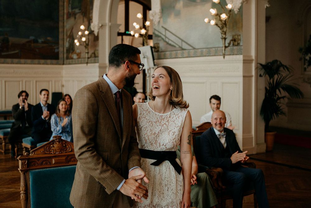Bride laughs joyfully with groom after wedding ceremony in an elegant chandelier-lit room.