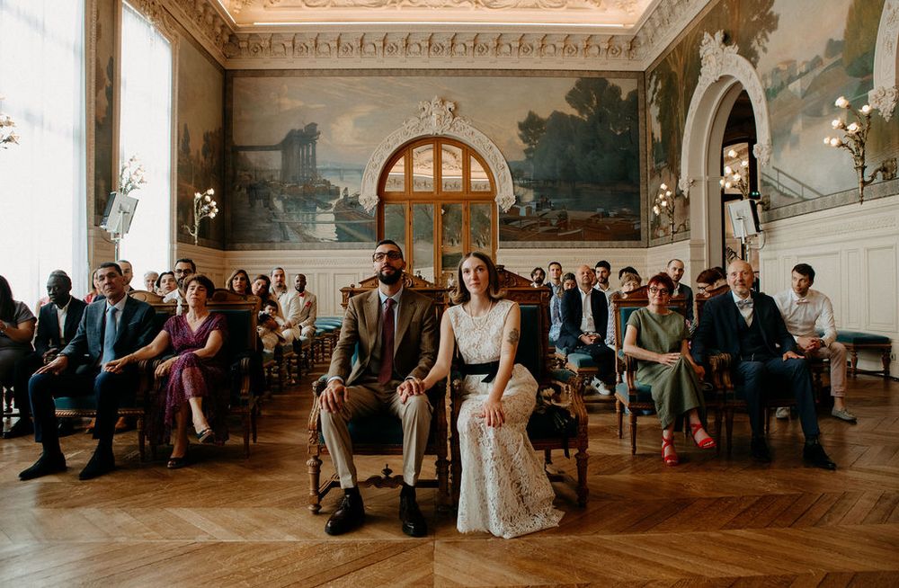 Bride and groom sit together during civil wedding ceremony in an ornate frescoed hall.