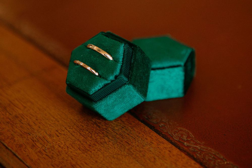 Two gold wedding bands displayed in a teal velvet geometric ring box on wood.