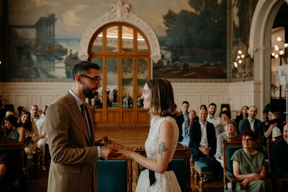 Bride and groom exchange rings during an intimate civil ceremony with guests seated behind.