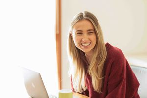 Young woman laughing in a room with a computer on the desk.
