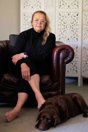 Woman sitting in leather chair with chocolate labrador dog at her feet.