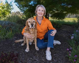 woman in orange shirt sitting in garden with her dog