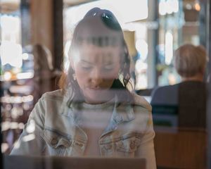 Young woman sitting inside cafe taken through window.