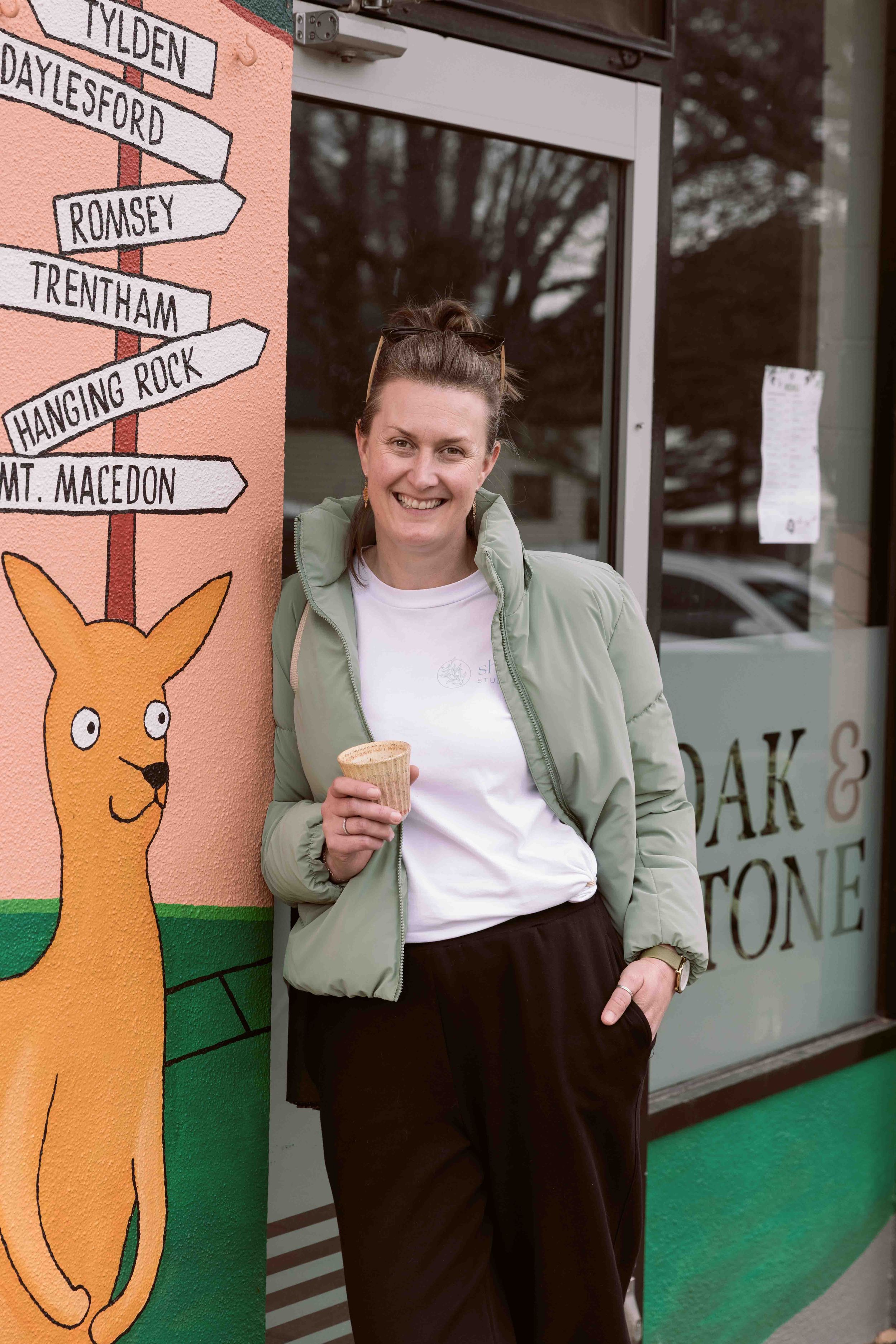 Woman in Casula clothes leaning against wall with a coffee in hand