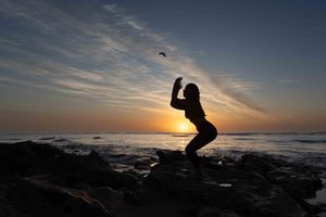 photo of young woman doing Yoga at sunrise at the beach