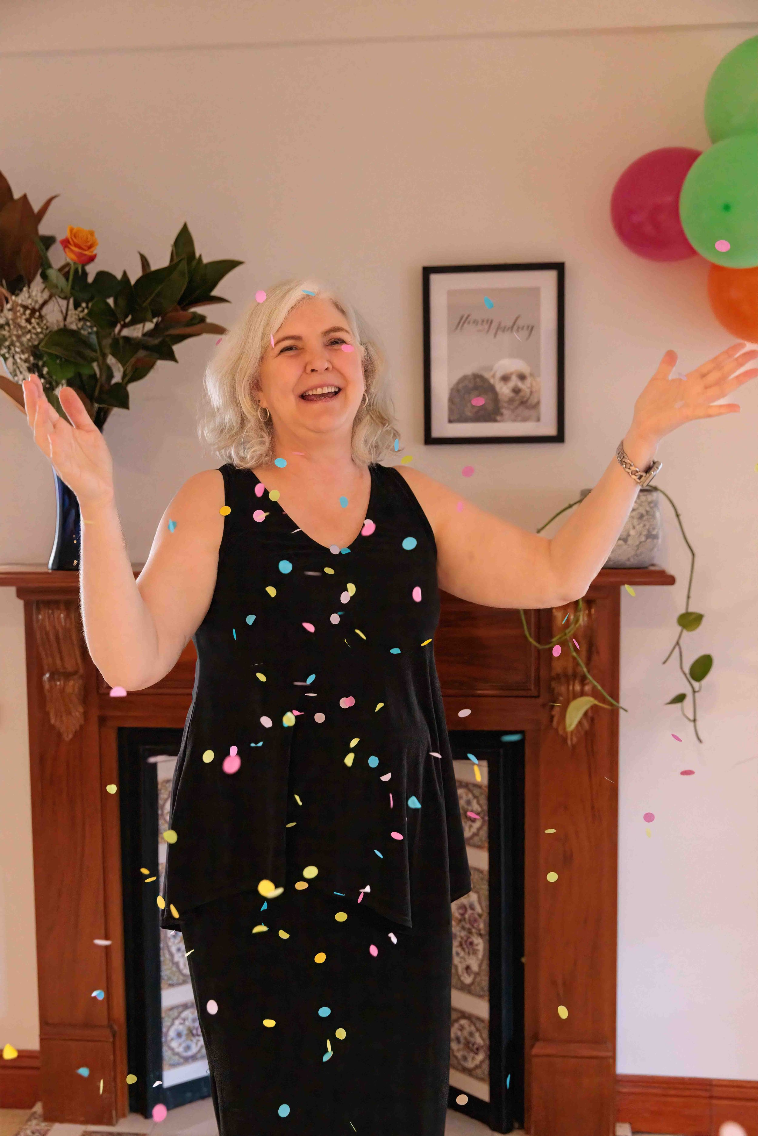 Woman celebrating throwing confetti with balloons nearby