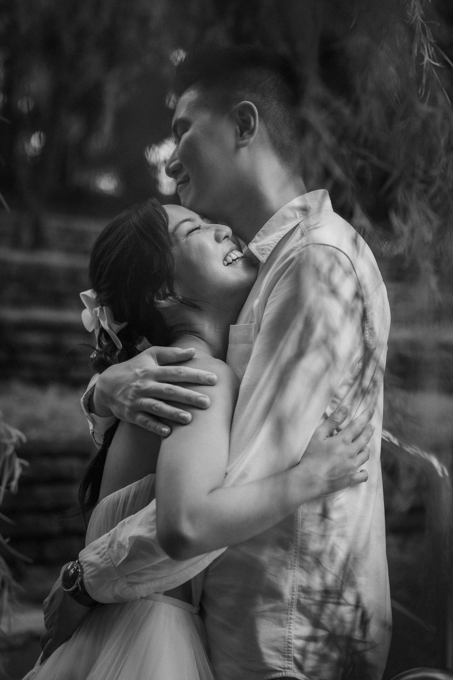 Black and white romantic portrait of a couple embracing and laughing together outdoors.