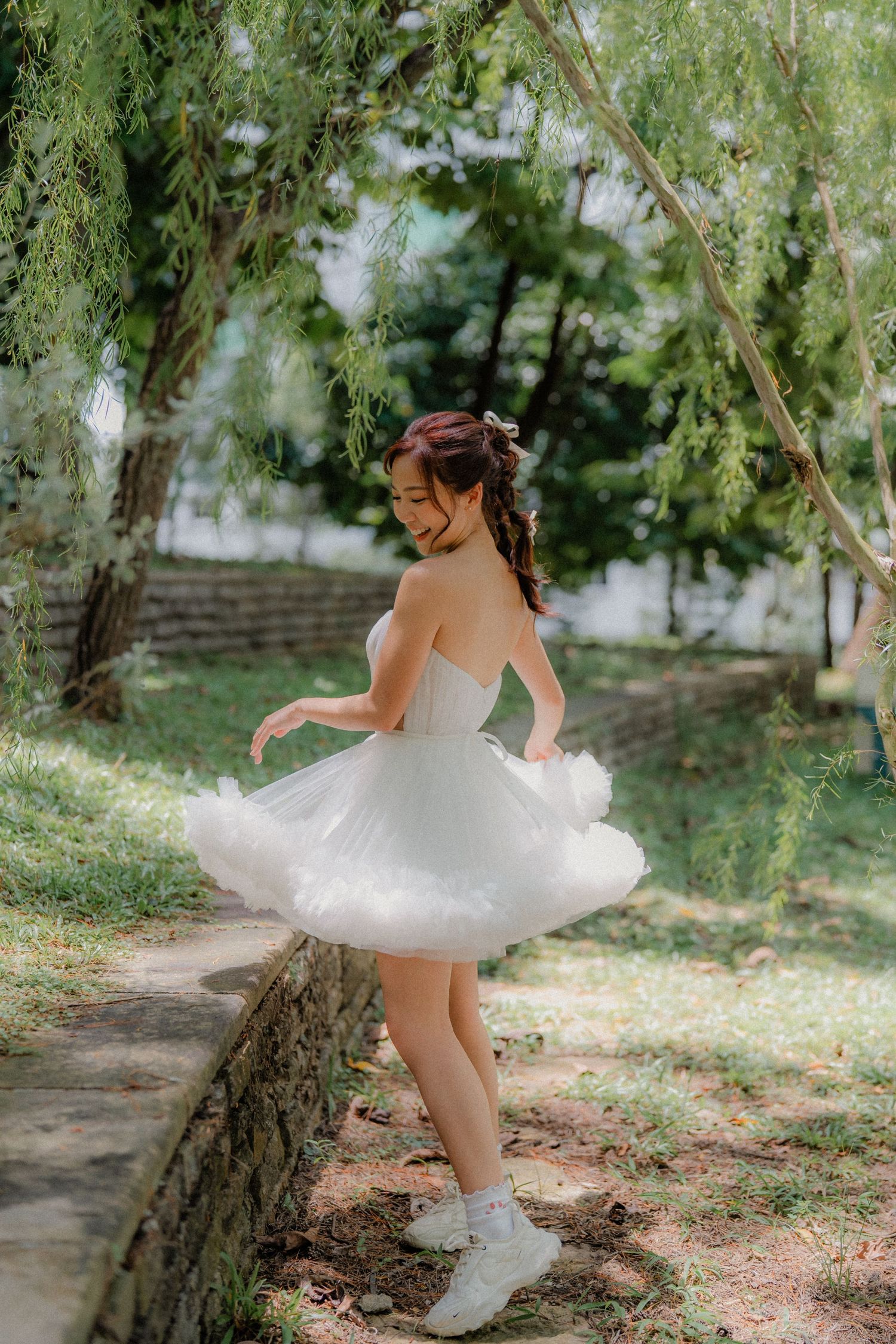 A little ballerina in a white tulle dress twirls playfully in a sunlit garden setting.