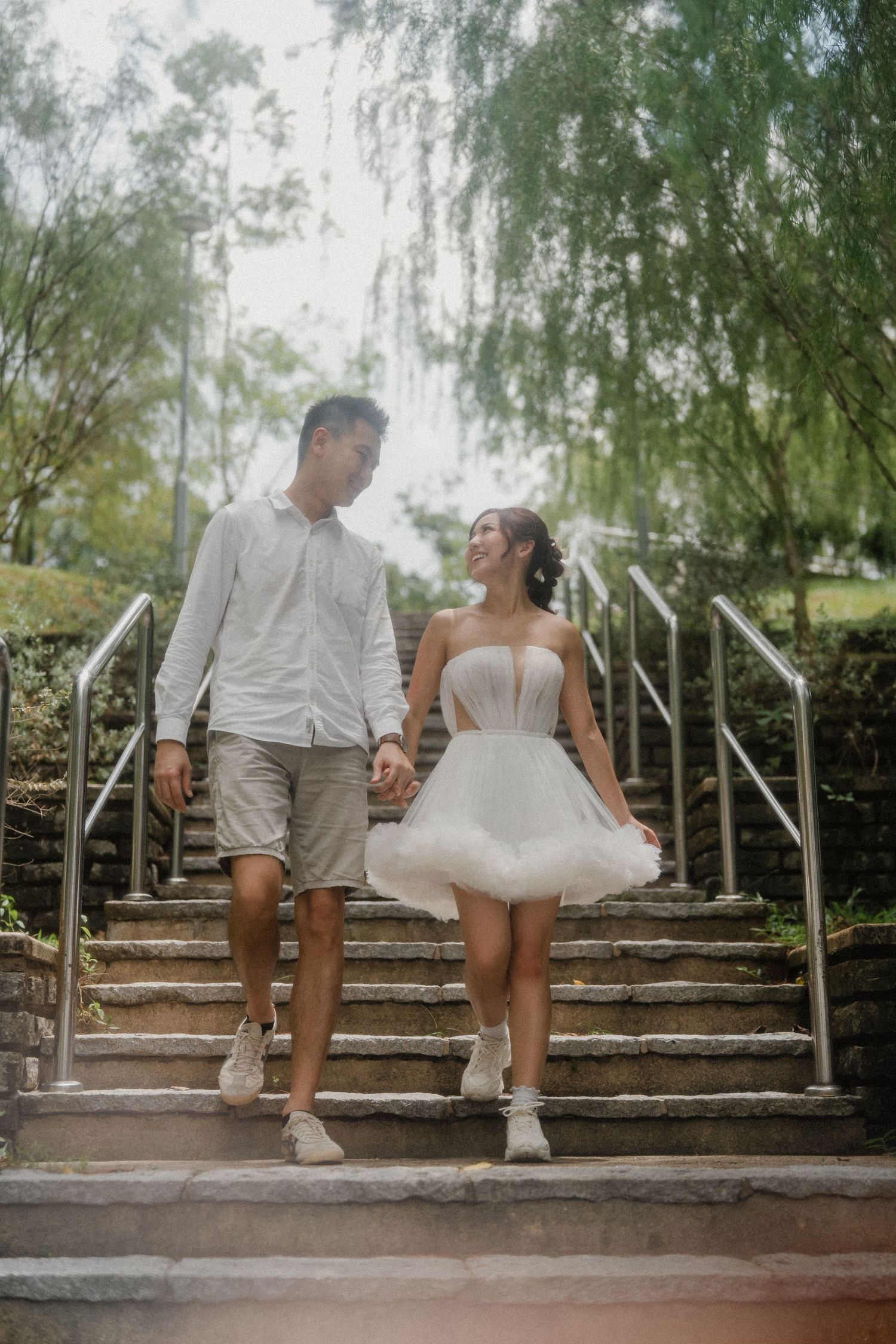 Couple sits together on rustic stone steps with overhanging willow branches creating a romantic wedding scene.