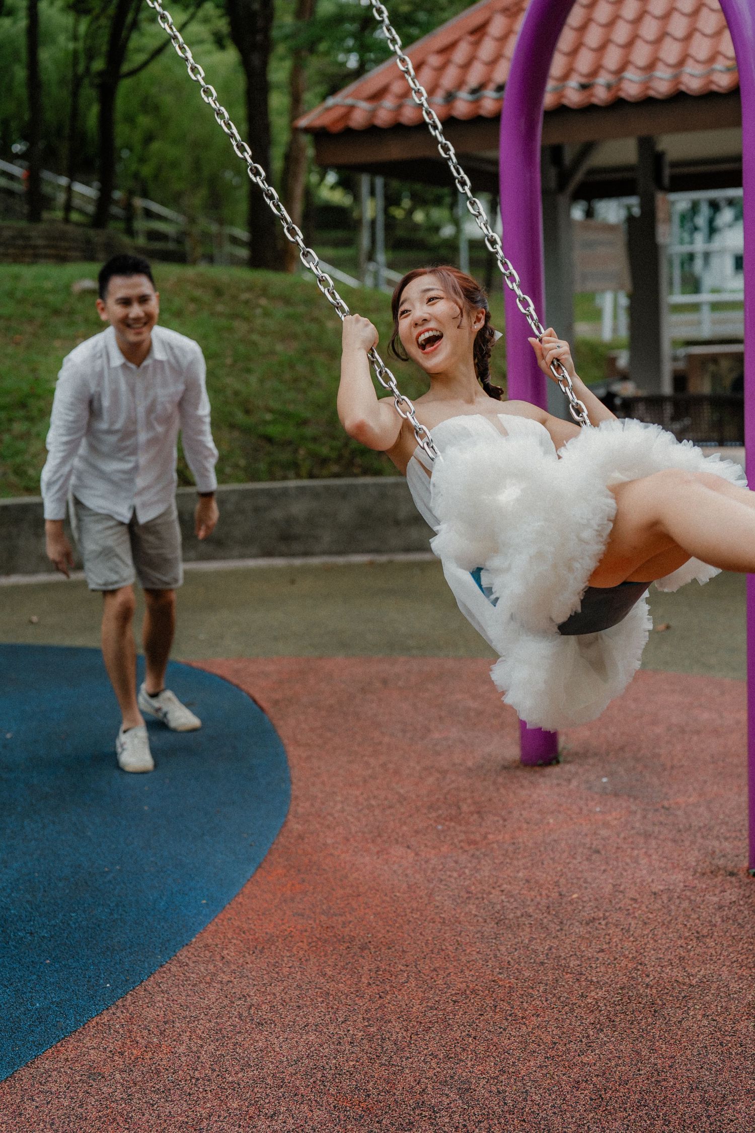 A joyful moment at a playground as someone wearing a white dress swings while someone in a light shirt watches.